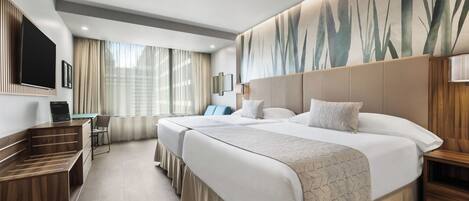 A hotel room with two beds, a desk, a chair, and a TV.