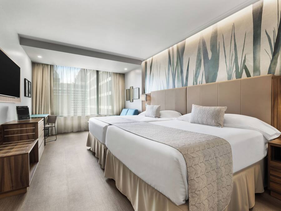 A hotel room with two beds, a desk, a chair, and a TV.