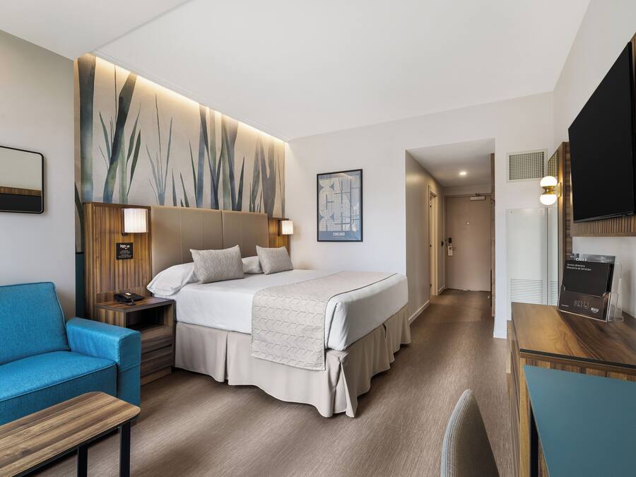 Une chambre d’hôtel avec un lit, un canapé bleu, un bureau avec un téléviseur à écran plat et une œuvre d’art accrochée au mur.