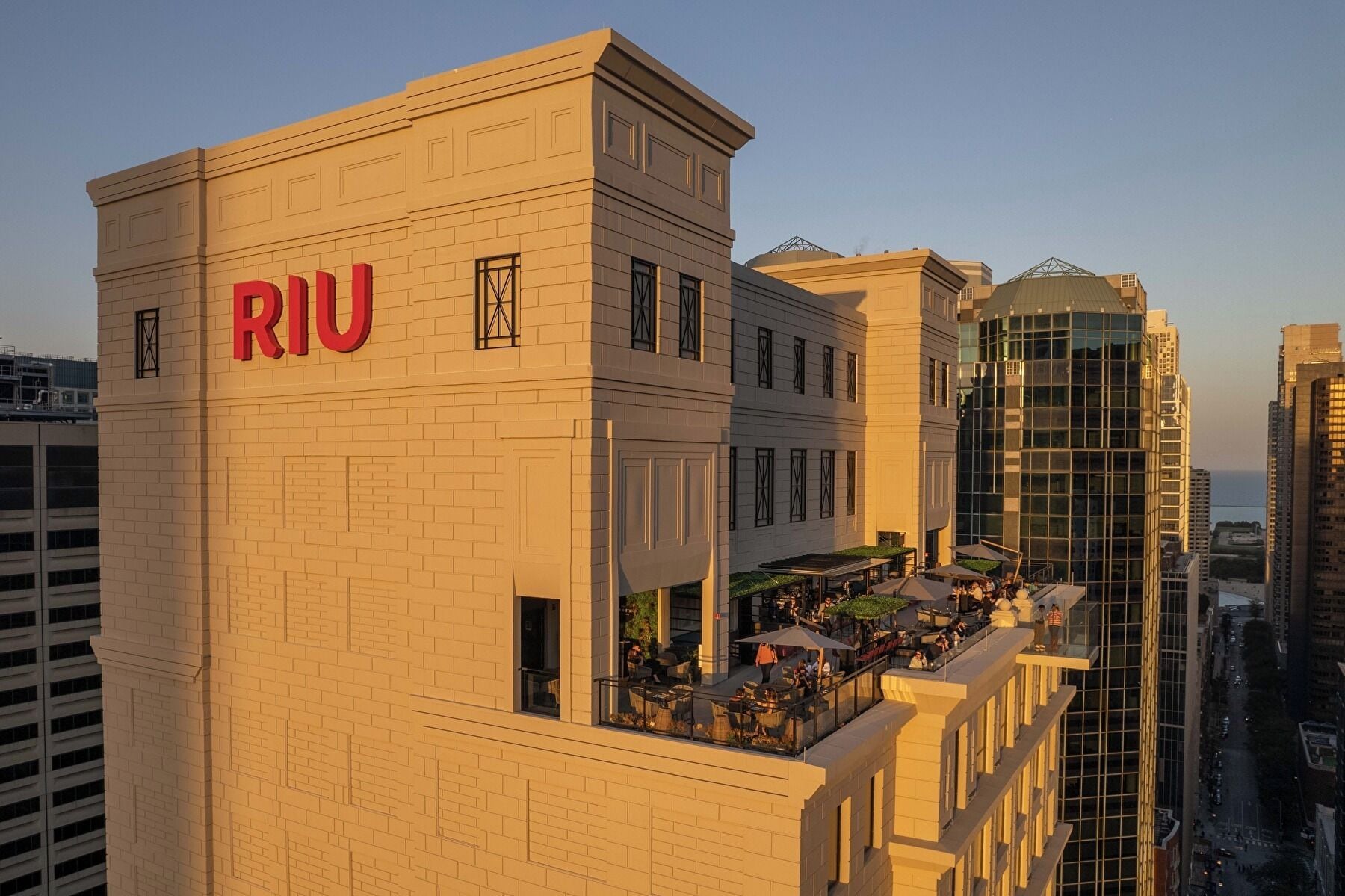 Un hôtel avec une enseigne « RIU » bien visible, un bar sur le toit doté d’une terrasse, et un bâtiment moderne en verre en arrière-plan.