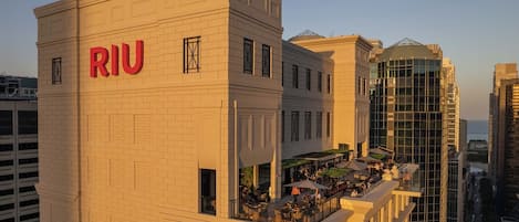 Un hôtel avec une enseigne « RIU » bien visible, un bar sur le toit doté d’une terrasse, et un bâtiment moderne en verre en arrière-plan.