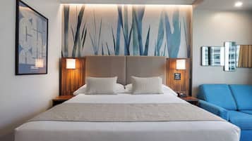 Una camera d'albergo con un letto grande, due comodini con lampade, una poltrona blu e una parete decorata con un paesaggio urbano e arte astratta.