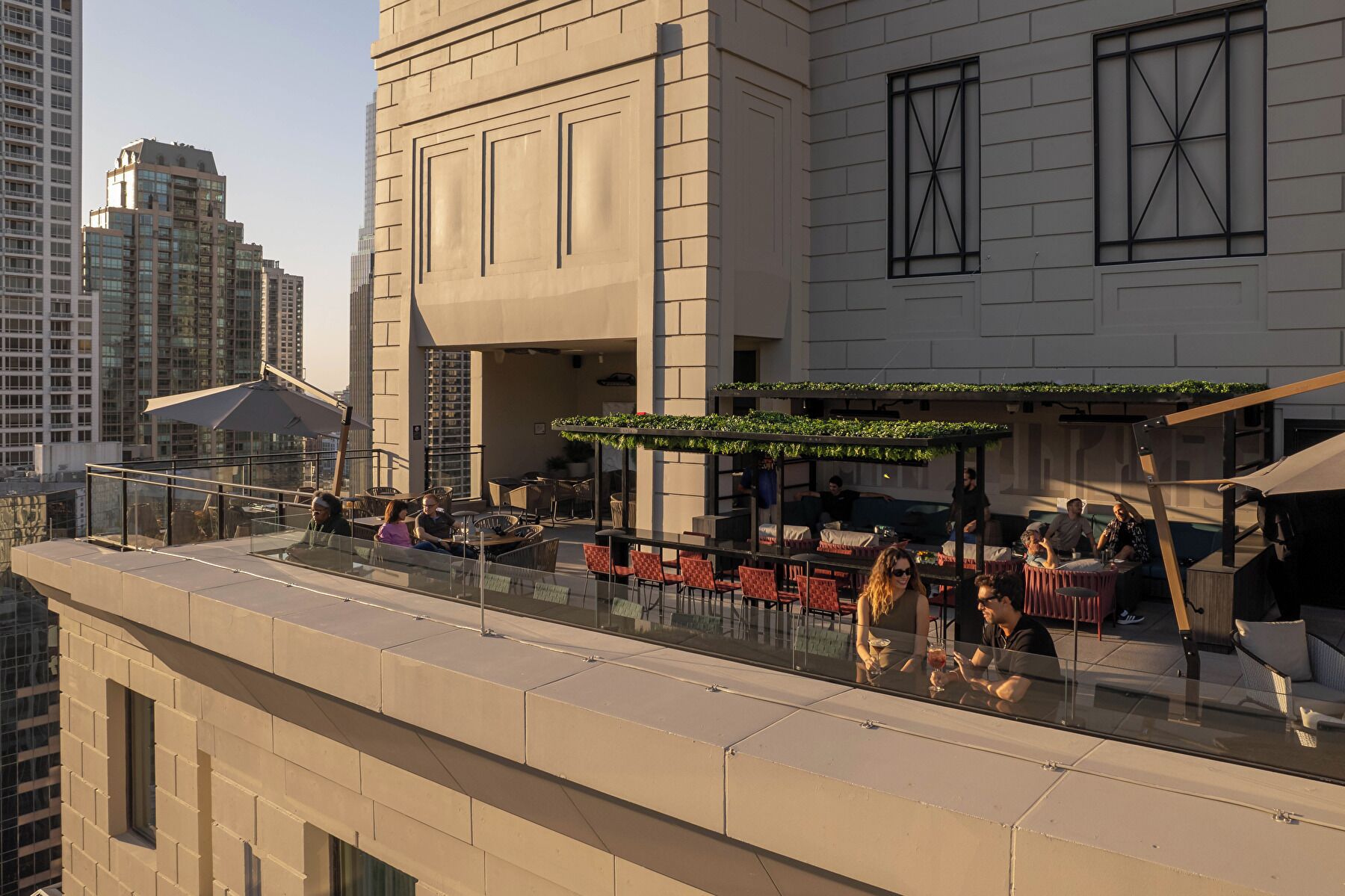 Um bar no terraço com área externa, guarda-corpo de vidro e vista para o horizonte da cidade.