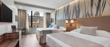 A hotel room with two beds, a desk, a chair, and a large window offering a city view.