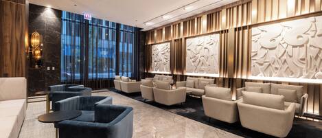 A modern lobby with a marble floor, sofas, and armchairs arranged for seating.