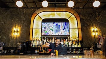 Zona de bar con un bartender preparando una bebida, una pantalla grande mostrando un paisaje urbano y una barra bien surtida con varias botellas.