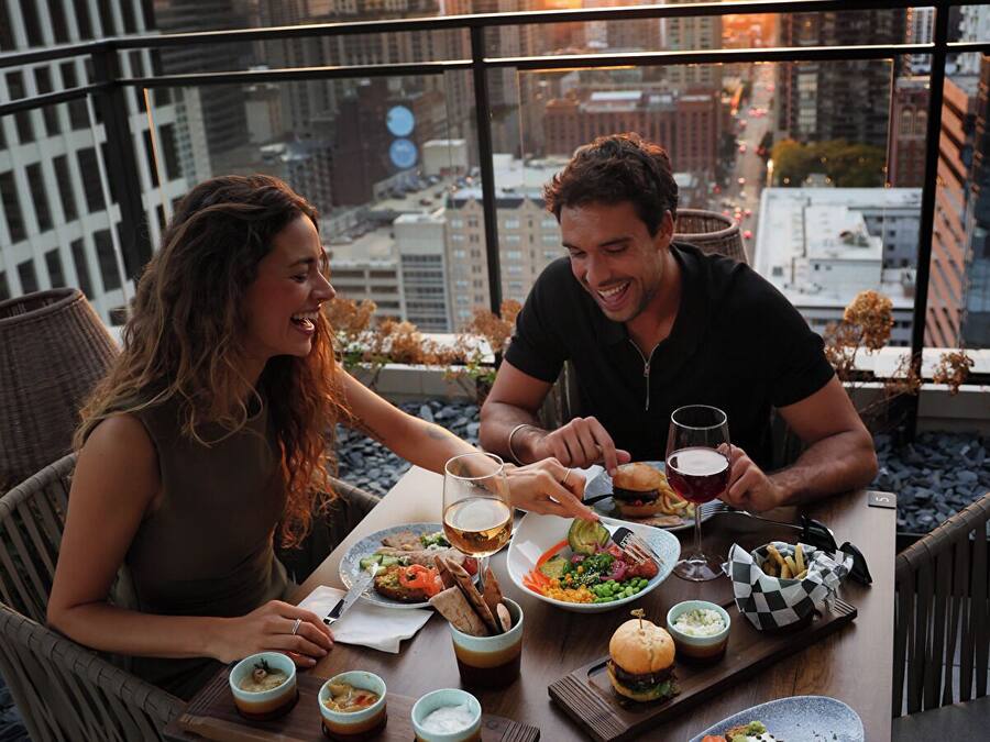 Una pareja cenando en una mesa con vista a la ciudad, rodeada de sillas y una variedad de platos.