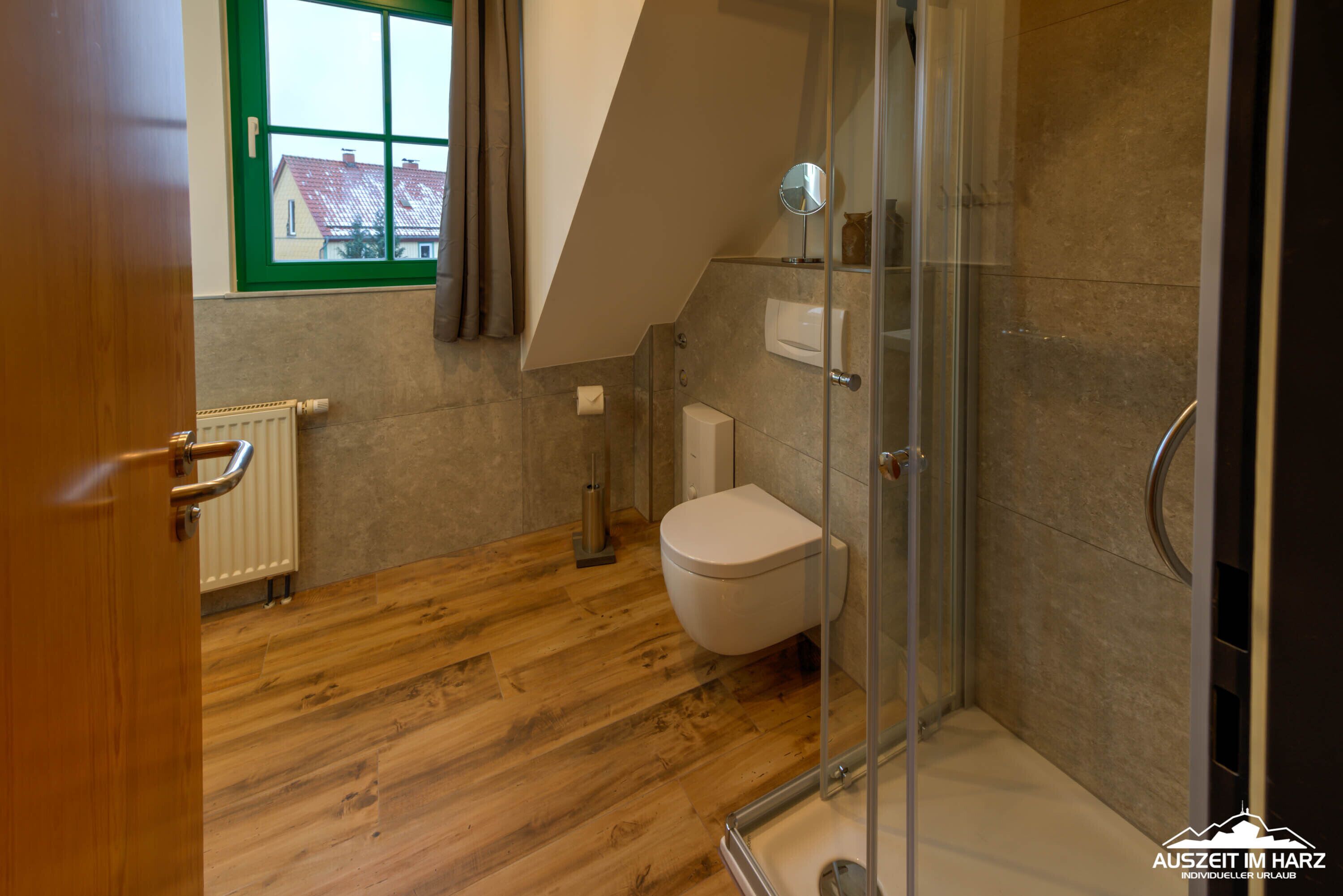 A modern bathroom with a wooden floor, a glass shower enclosure, and a white toilet.