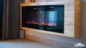 Una chimenea moderna con frente de vidrio, estructura de madera y objetos decorativos encima.