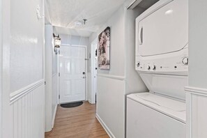 A laundry room with a front-loading washer and dryer, a wooden floor, and a door leading to another room. - 3 Bdrm Oceanfront Condo- 4 Bds- Pool- Near Main St (North Myrtle Beach)