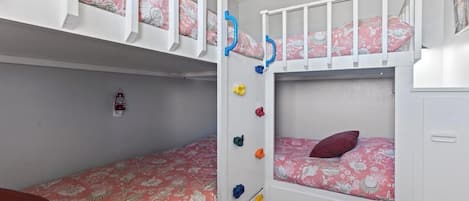 A bunk bed room with a lower bunk and a top bunk, both with floral bedding. There are colorful storage hooks on the wall.