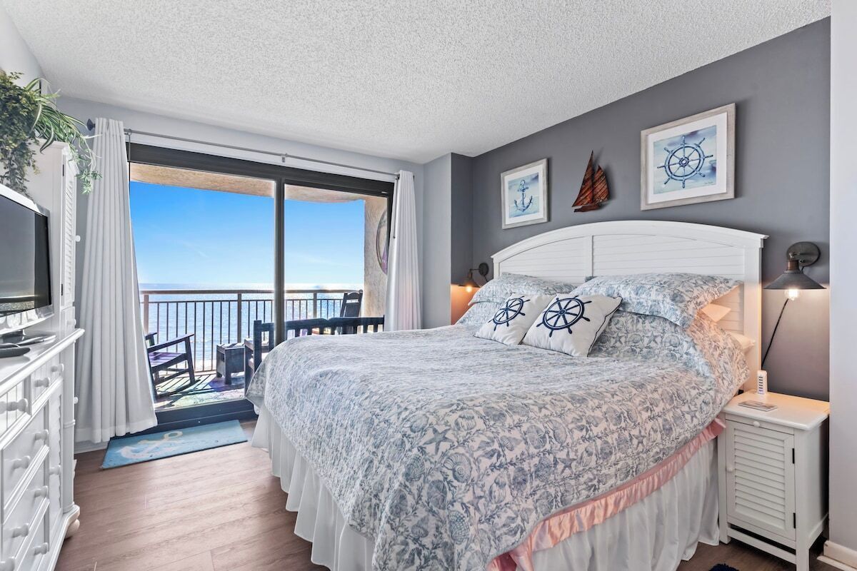 A bedroom with a bed, a TV, a desk, and a balcony with a view.