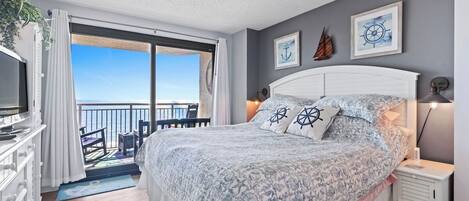 A bedroom with a bed, a TV, a desk, and a balcony with a view.
