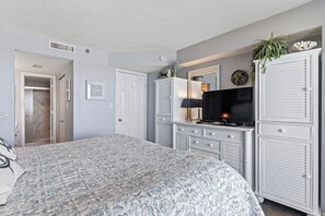 A bedroom with a large bed, a TV, a wardrobe, and a door leading to a bathroom. - 3 Bdrm Oceanfront Condo- 4 Bds- Pool- Near Main St (North Myrtle Beach)