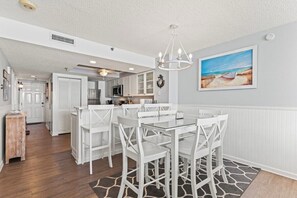 A modern kitchen with white cabinetry, a glass dining table, and a pendant light. - 3 Bdrm Oceanfront Condo- 4 Bds- Pool- Near Main St (North Myrtle Beach)