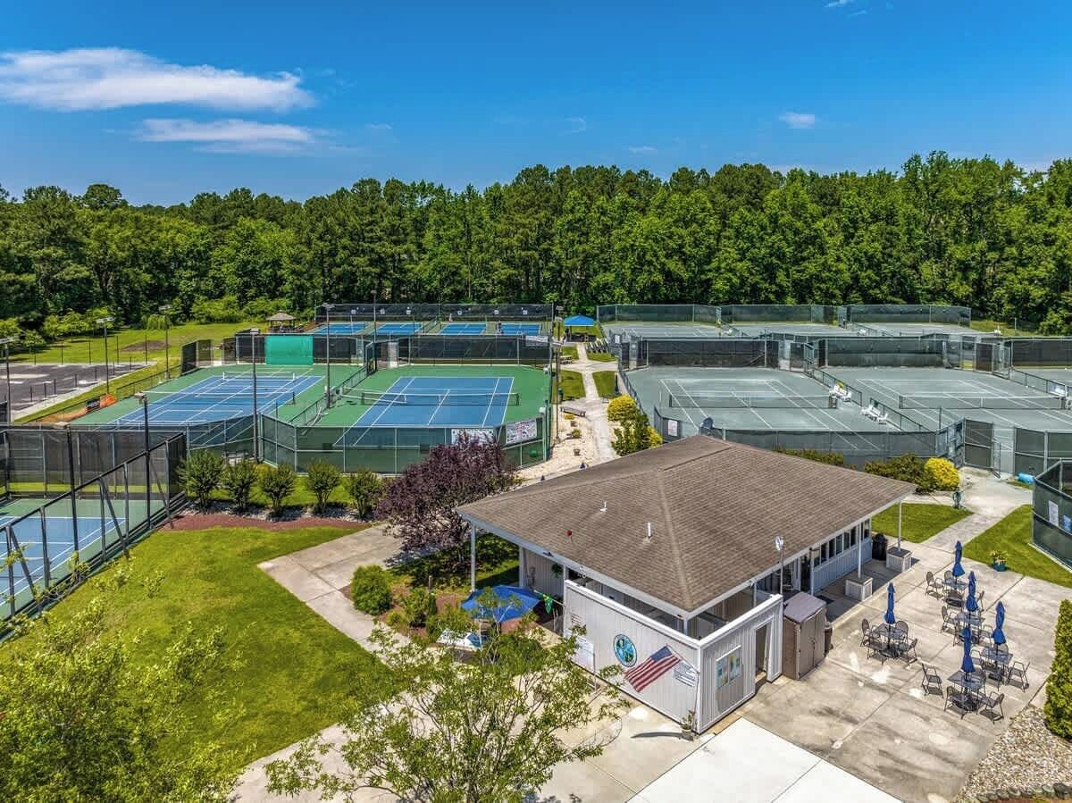 A sports complex with multiple tennis courts, a covered seating area, and a building with an American flag.
