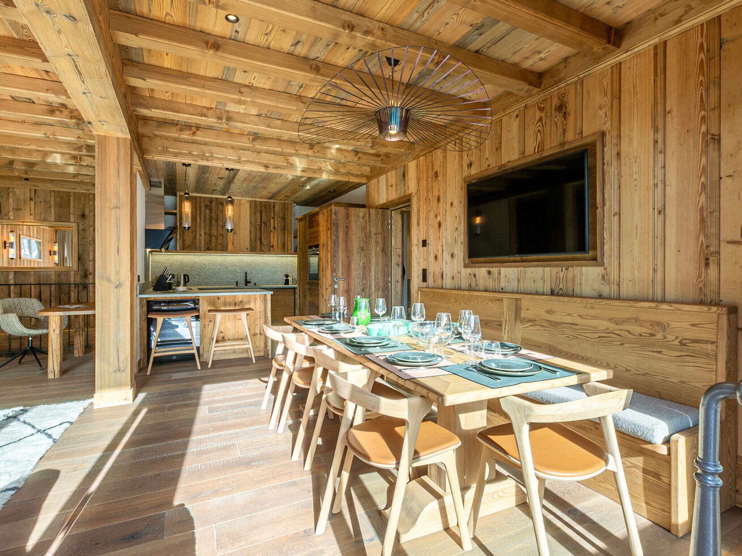 Interno di una baita in legno con zona pranzo, cucina e una grande finestra.