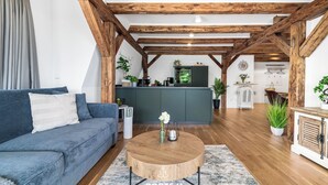 Una sala de estar moderna con un sofá azul, una mesa de centro de madera y una cocina al fondo.