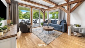 Ein modernes Wohnzimmer mit Holzbalken, einer Couch, einem Couchtisch und Blick durch große Fenster.