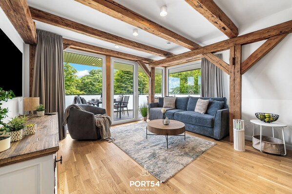 Un salon moderne avec des poutres en bois, un canapé, une table basse et une vue dégagée sur l’extérieur grâce à de grandes fenêtres.
