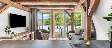 A modern kitchen with a black countertop and a sink, wooden beams on the ceiling, and a large window with a view of greenery.