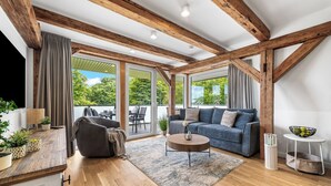 Una sala de estar moderna con vigas de madera, un sofá, una mesa de centro y vistas amplias a través de grandes ventanales.