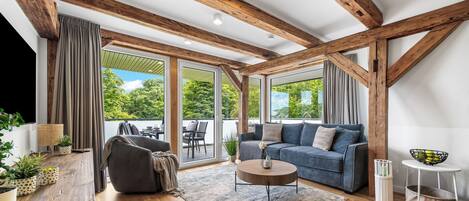 A modern living room with wooden beams, a sofa, a coffee table, and a view through large windows.