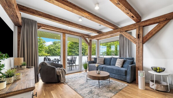 Una sala de estar moderna con vigas de madera, un sofá, una mesa de centro y vistas amplias a través de grandes ventanales.