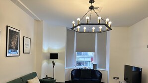 A modern living room with a green sofa, a dark blue sofa, a chandelier, a flat-screen TV, and a patterned rug. - Captivating 2-bed Apartment in Brighton (Brighton)