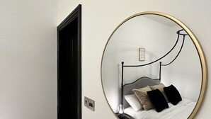 A bedroom with a round mirror, a bed with white and black bedding, a bedside table, and a wall-mounted light fixture. - Captivating 2-bed Apartment in Brighton (Brighton)