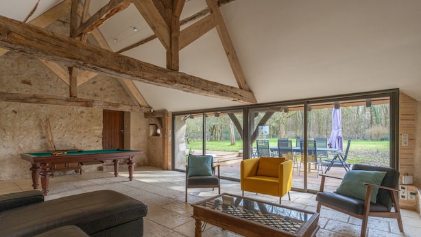 Una habitación amplia con mesa de billar, mesa de futbolín y una mesa de centro. Hay dos sillones y un sofá. La habitación tiene ventanas grandes con vistas al exterior.