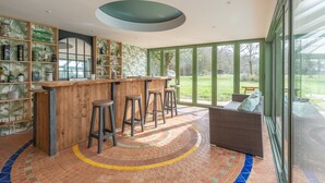 Zona de bar moderna con taburetes de madera, suelo con estampado de ladrillo y un ventanal con vistas al exterior.
