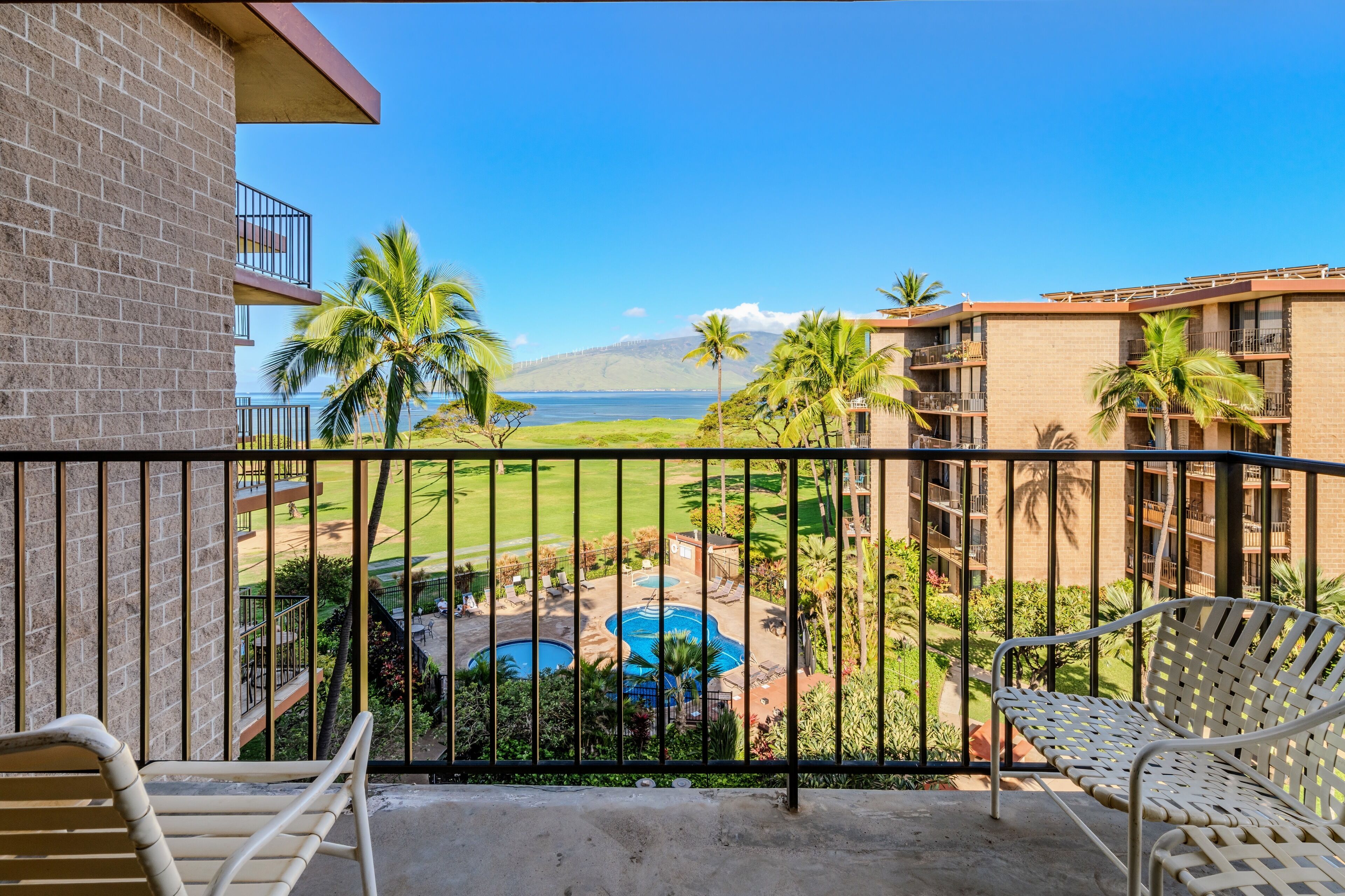 A balcony with a view of a golf course, a pool, and a mountain.