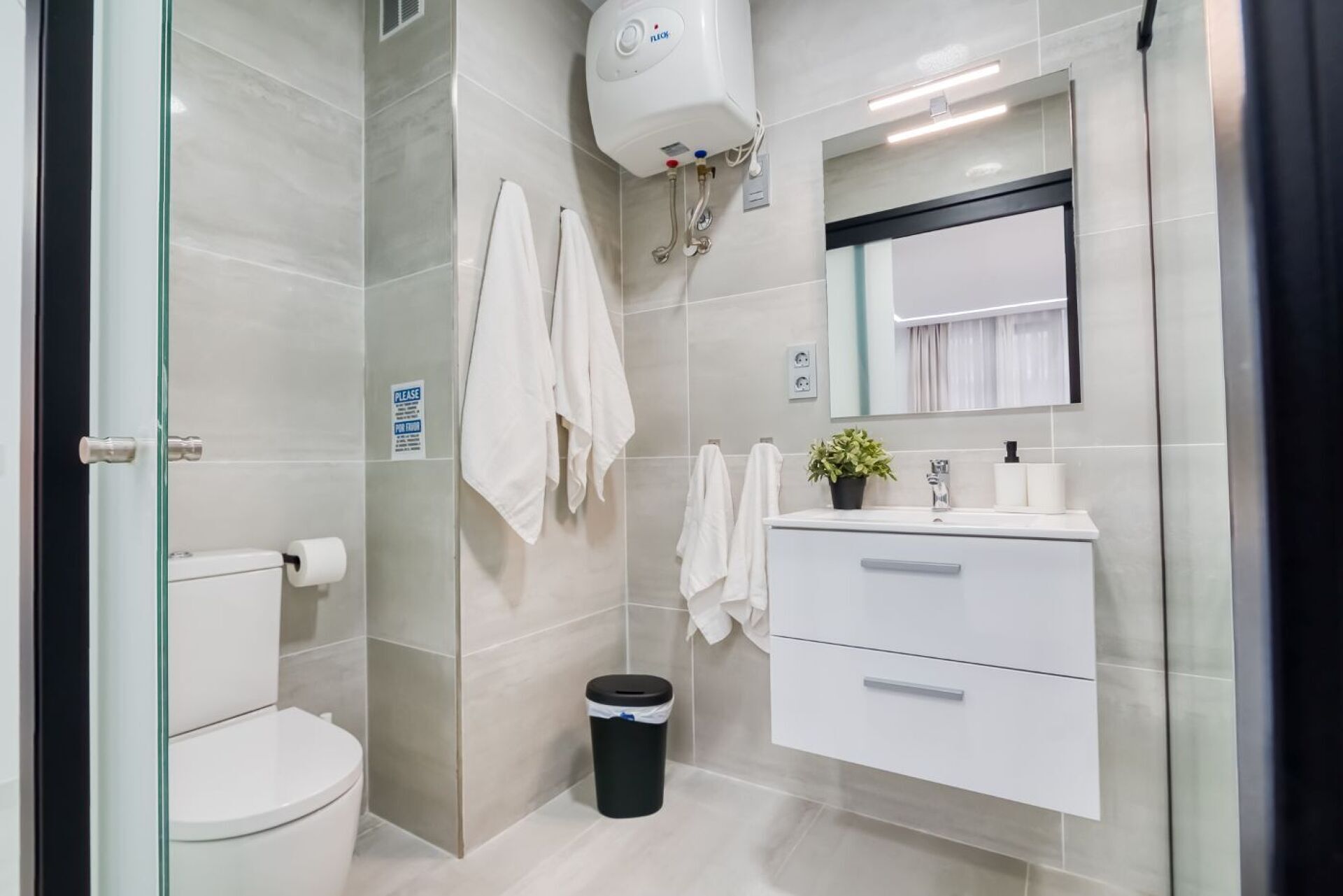 A modern bathroom with a toilet, a sink with a mirror, a towel rack, and a trash bin.