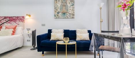 Un salon moderne avec un canapé bleu, une table ronde dorée et un tableau décoratif accroché au mur.