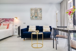 Un salon moderne avec un canapé bleu, une table ronde dorée et un tableau décoratif accroché au mur.