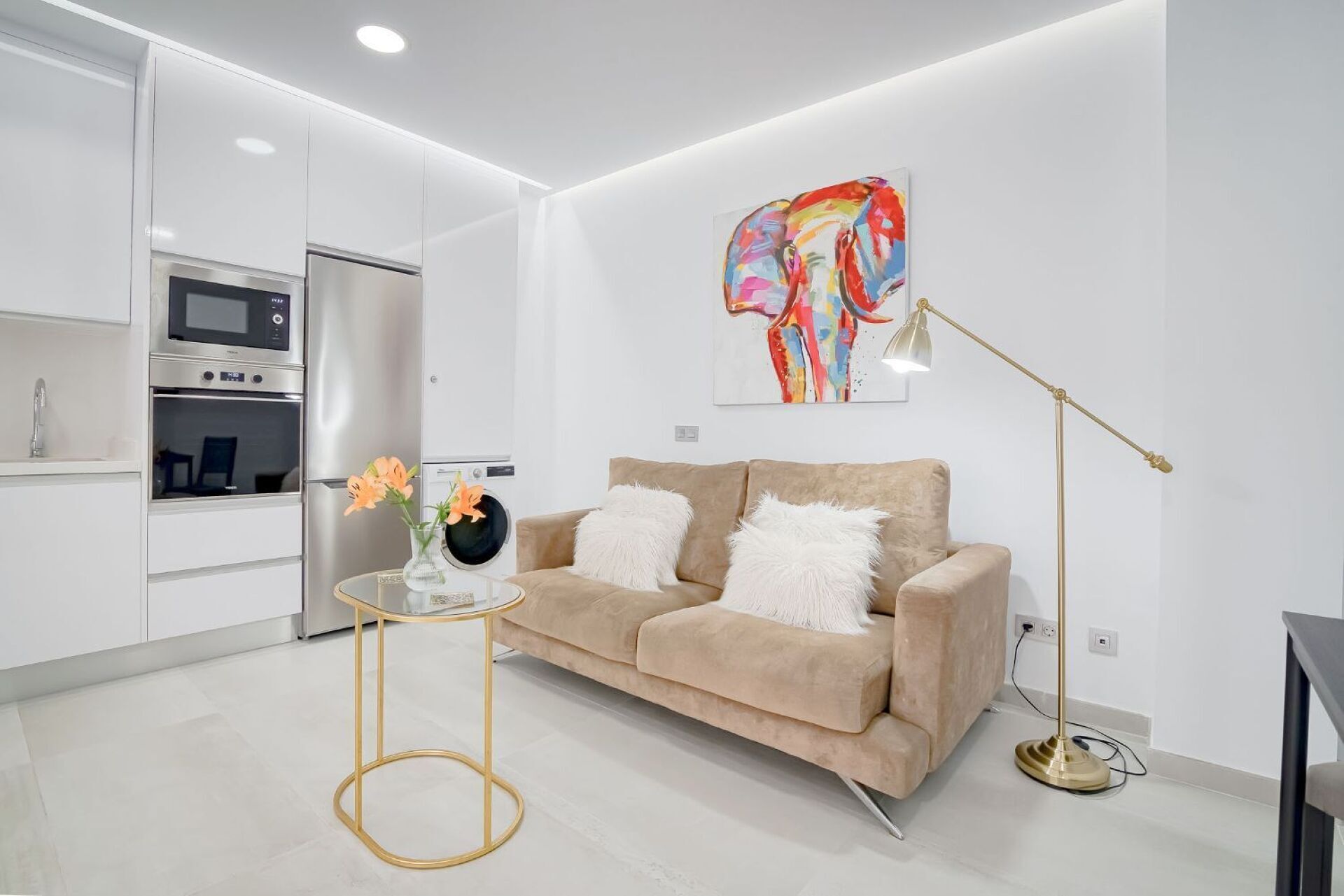 A modern living room with a sofa, a coffee table, a floor lamp, and a kitchen area with appliances.