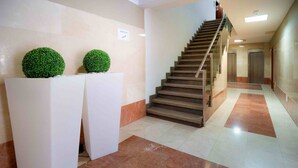 Un moderno vestíbulo de hotel con suelo de mármol, una escalera y dos plantas esféricas verdes sobre pedestales blancos.