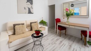 Una sala de estar moderna con un sofá, una mesita redonda, un escritorio con una silla, un espejo y una planta en maceta.