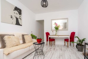 A modern living room with a white sofa, a dining table, red chairs, and a mirror above the table.