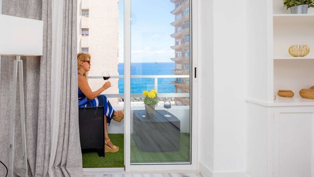 Una habitación con puerta de cristal corredera que da a un balcón con vistas al mar.