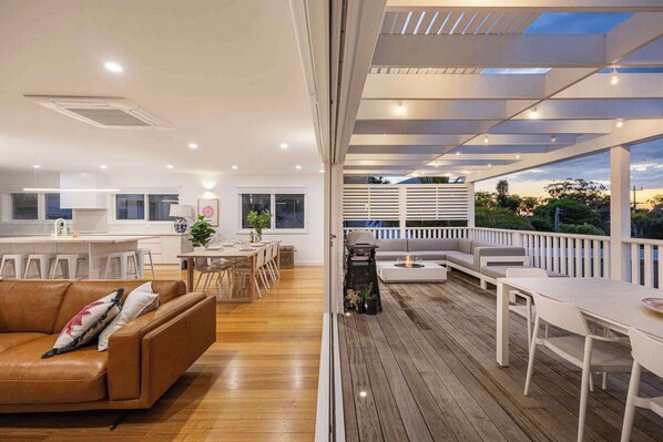 A spacious living area with a wooden floor, a brown leather sofa, a dining table with chairs, and a barbecue grill.