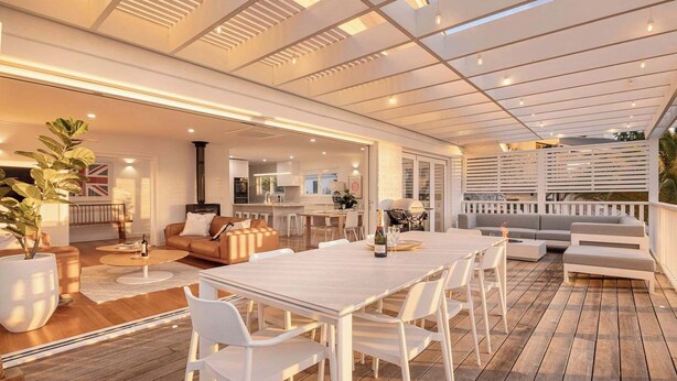 Een terras buiten met een houten dek, witte meubels en uitzicht op het interieur.