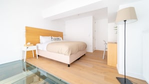 Une chambre à coucher moderne avec une table basse en verre, un lit doté d’une tête de lit en bois, une table de chevet et une lampe sur pied.