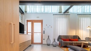 Un salon moderne avec un canapé, une table basse et un téléviseur posé sur un meuble en bois. On peut voir deux vases sur le sol et une lampe sur la droite.