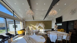 Un comedor espacioso con varias mesas dispuestas para un evento formal, con candelabros elegantes y vistas al exterior.