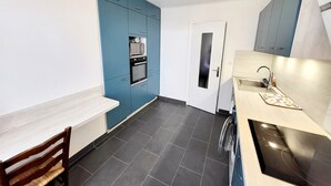 Uma cozinha compacta com armários azuis, porta branca, forno embutido e uma pia moderna.