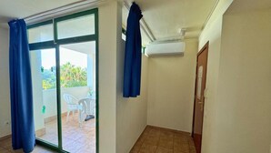 Une pièce dotée d’une porte-fenêtre coulissante donnant sur un balcon, d’un climatiseur blanc fixé au mur et d’une porte en bois.