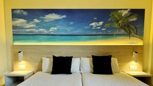 Une chambre d’hôtel avec un lit, deux tables de chevet et un grand tableau représentant une scène de plage.