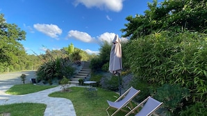 Un giardino con vialetto lastricato, due poltrone da relax e un ombrellone.